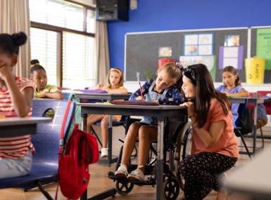 Diverse female teacher and schoolgirl in wheelchair in elementary school class