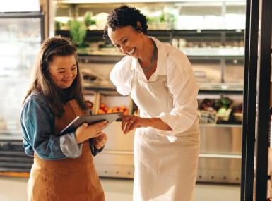 Convenience store workers using a digital tablet together, one employee has downsydrome