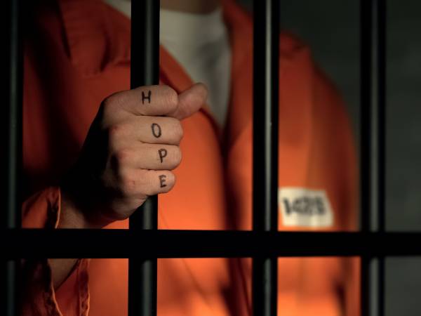 Hope word on imprisoned man fingers, holding jail bars, dream about freedom