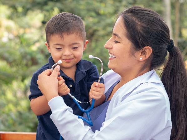Portrait of a doctor and a child with Down syndrome smiling together.