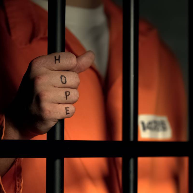 Hope word on imprisoned man fingers, holding jail bars, dream about freedom