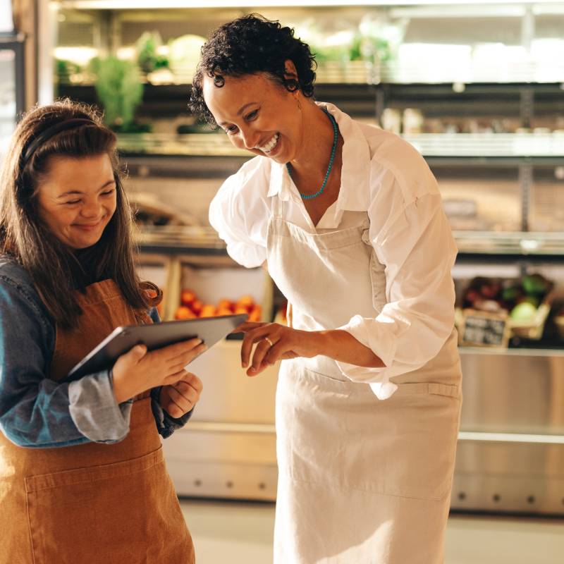 Convenience store workers using a digital tablet together, one employee has downsydrome