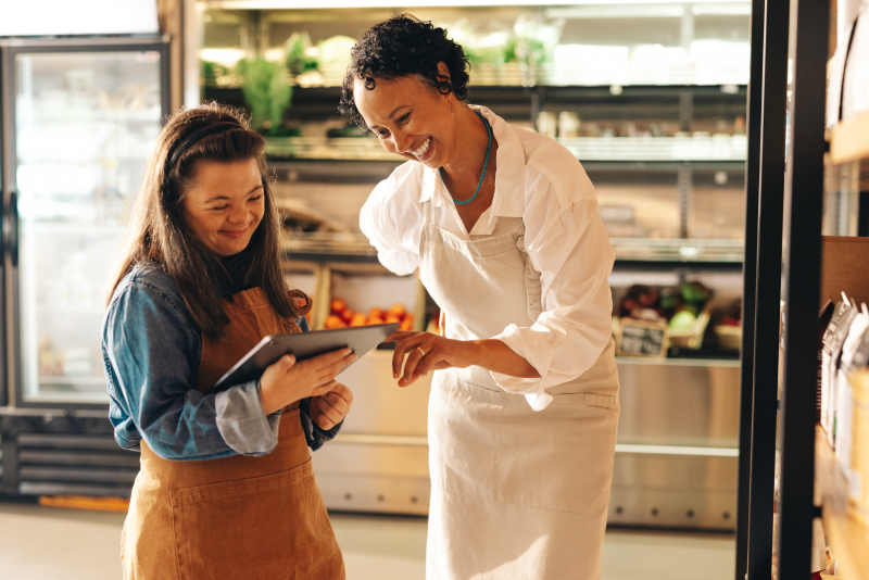 Convenience store workers using a digital tablet together, one employee has downsydrome