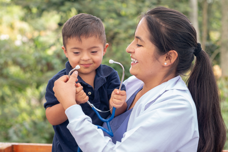 Portrait of a doctor and a child with Down syndrome smiling together.